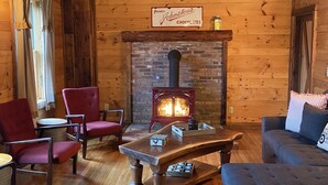 A cozy cabin interior with wooden walls, a brick fireplace, and a sign reading "Agency Johnstone's Chocolates."