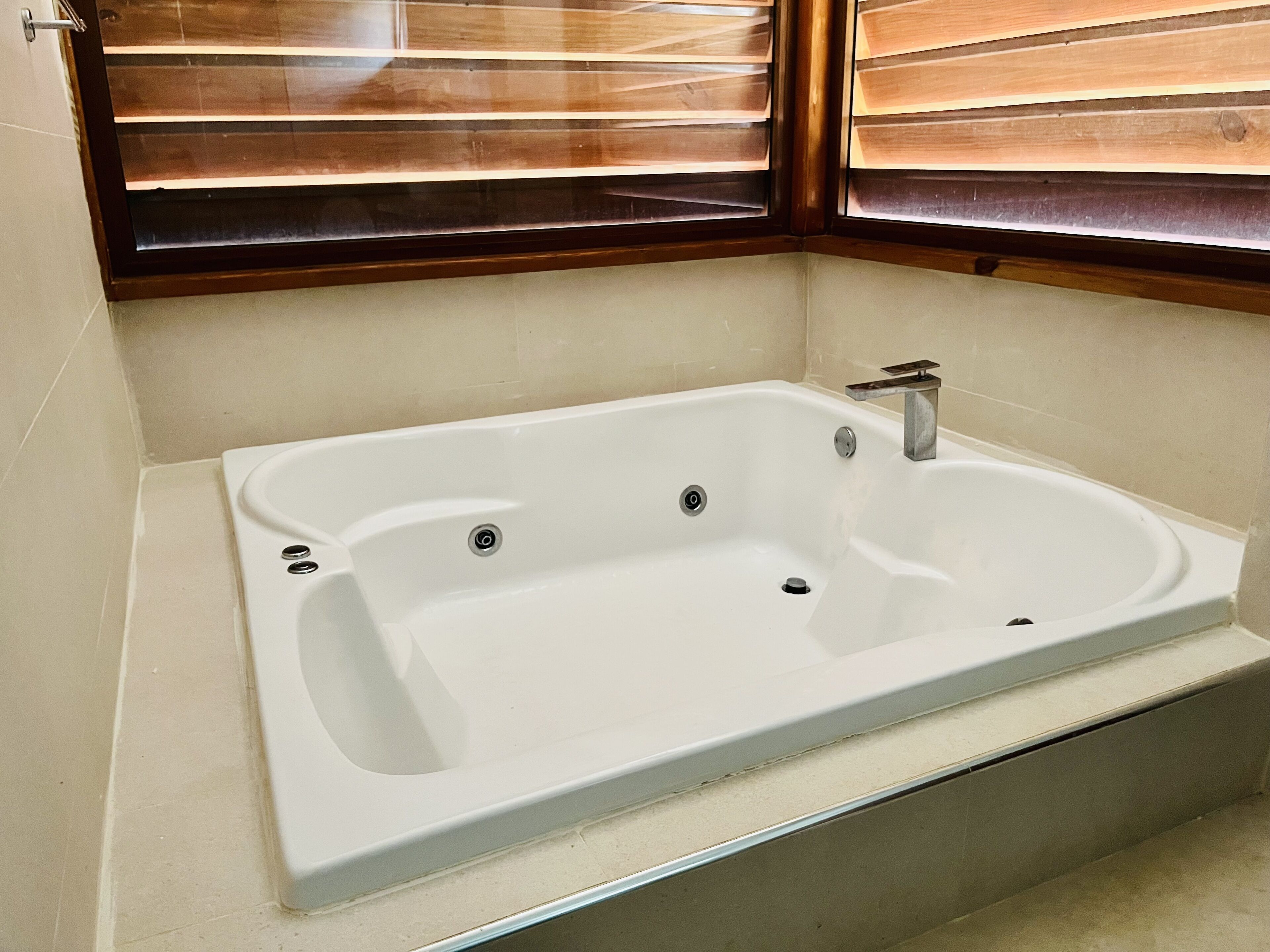 Ein modernes Badezimmer mit einer freistehenden Badewanne, einer Duschkabine und einem Fenster mit Jalousien.