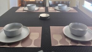 A dining table with plates and bowls, a window with blinds, and a kitchen area in the background. - By Popular Demand - Richmond (Richmond)