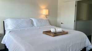 A neatly made bed with white linens, a bedside lamp, and a tray with a towel and remote control. - By Popular Demand - Richmond (Richmond)