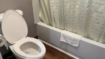 A bathroom with a white toilet, a shower curtain, and a towel hanging on the bathtub.