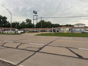 A motel with a signboard, a fenced parking area, and a building with a red roof. - RIVERSIDE MOTEL (Hebron)