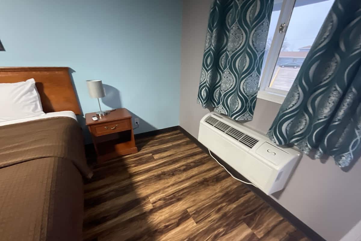 A room with a bed, a nightstand, a lamp, a heater, and patterned curtains.