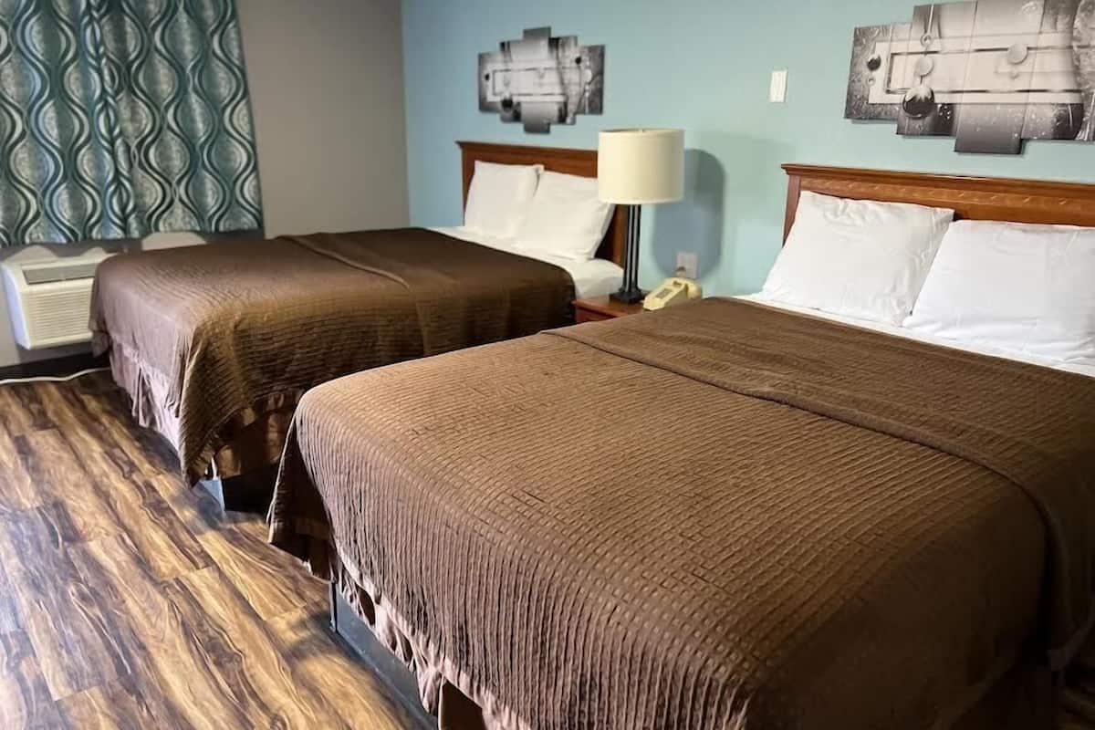 A hotel room with two beds, a patterned wall, a lamp, and a phone on the nightstand.