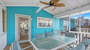 Katettu ulkotila, jossa on pöytä ja tuolit, kattotuuletin ja näkymä kaupunkiin.