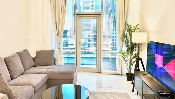 Una sala de estar moderna con un sofá, un televisor y vistas a un paisaje urbano a través de amplios ventanales.