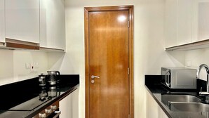 Cocina compacta con puerta de madera, encimeras negras, microondas y pileta.