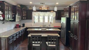 A kitchen with dark wood cabinets, granite countertops, a central island with chairs, and pendant lighting. - 5min Walk from Love beach | Spacious Home in Nassau (Nassau)