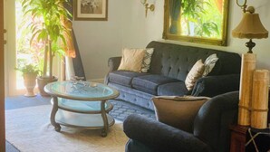 A living room with a dark blue sofa, a glass coffee table, and a lamp. There are potted plants and a framed picture on the wall. - 5min Walk from Love beach | Spacious Home in Nassau (Nassau)