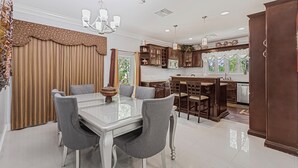 A modern kitchen with dark wooden cabinets, a central island, and a dining area with a glass table and grey chairs. - 5min Walk from Love beach | Spacious Home in Nassau (Nassau)