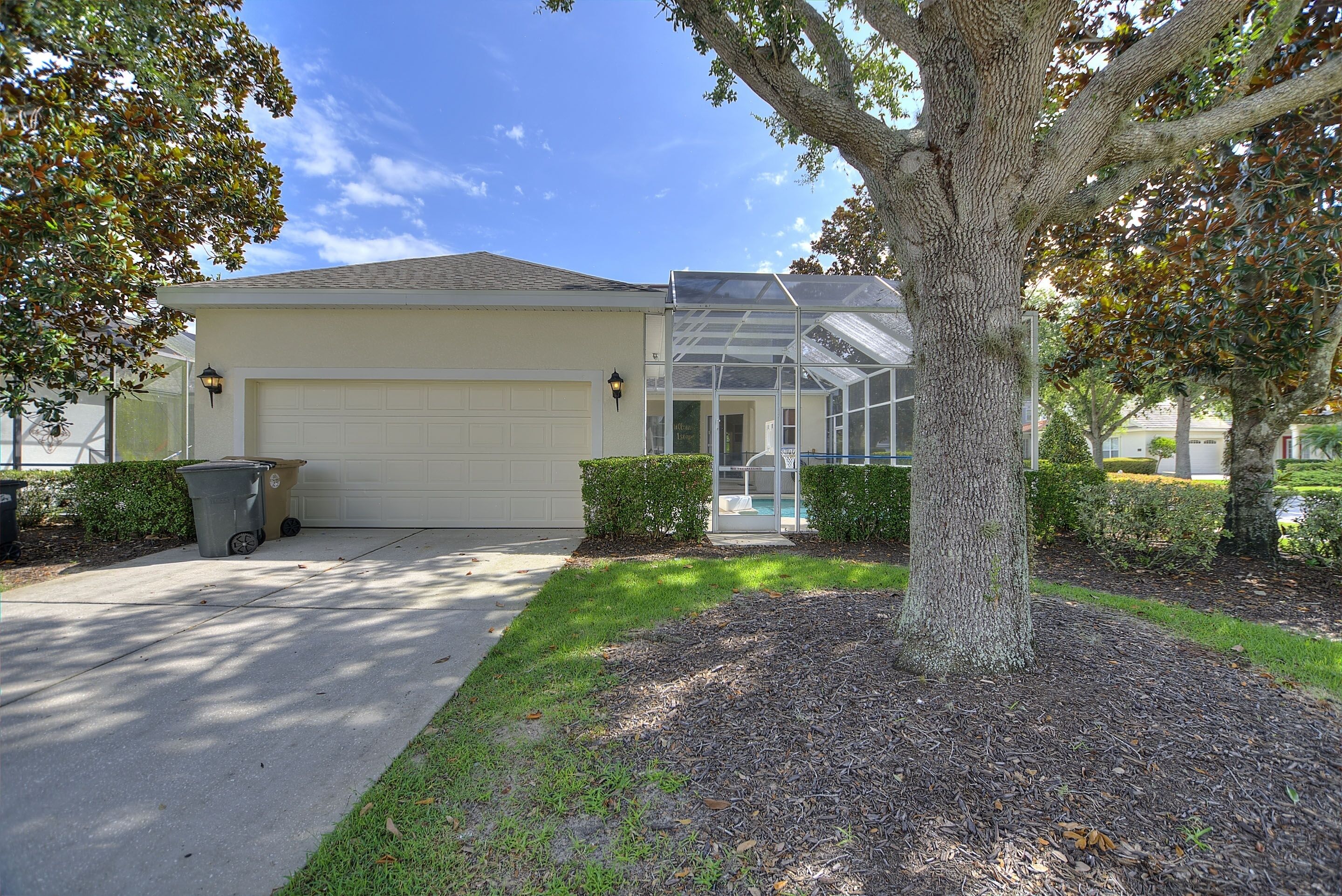 A residential house with a garage, a covered porch, and a large tree in the front yard.