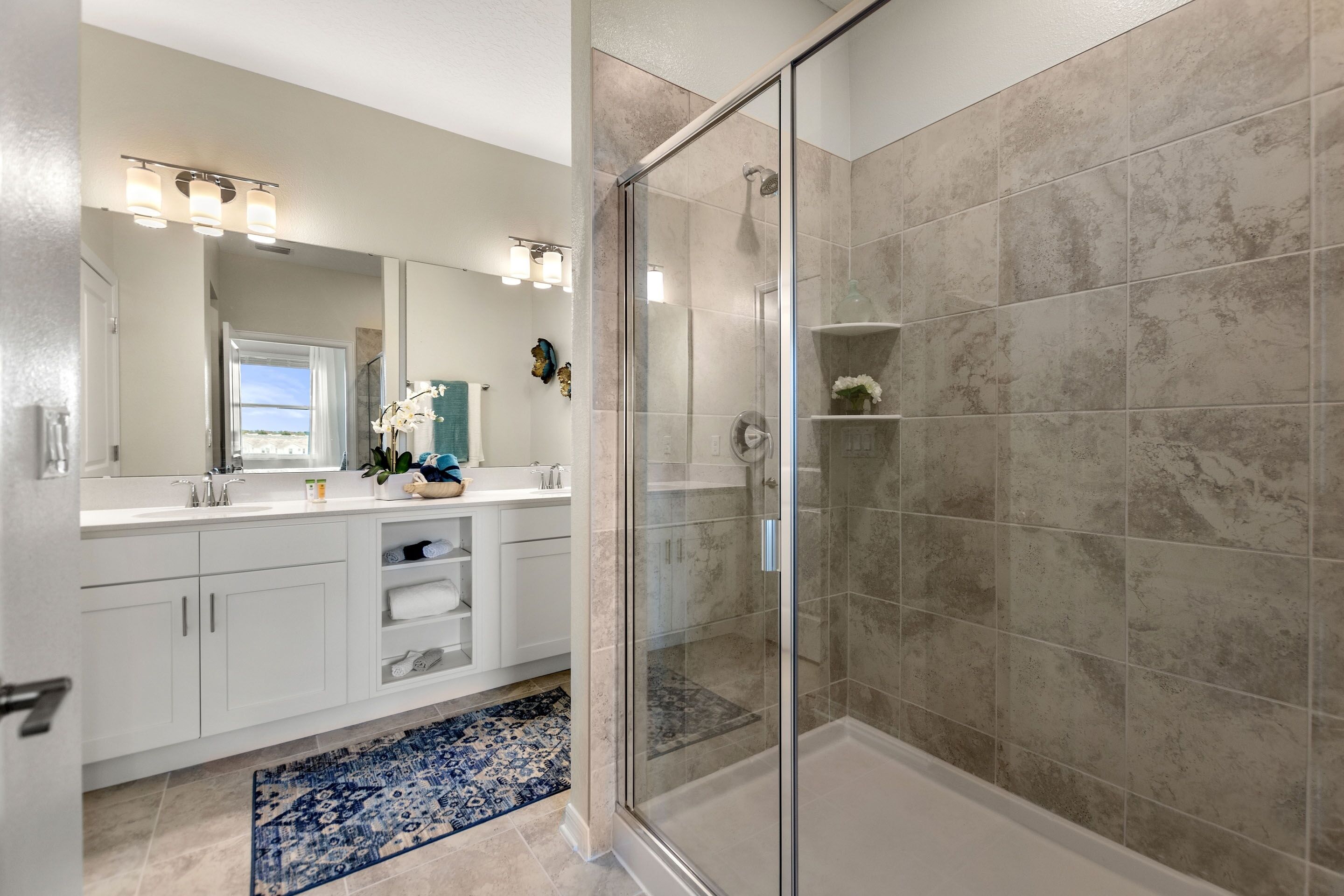 A modern bathroom with a glass-enclosed shower, white cabinetry, and a decorative rug.