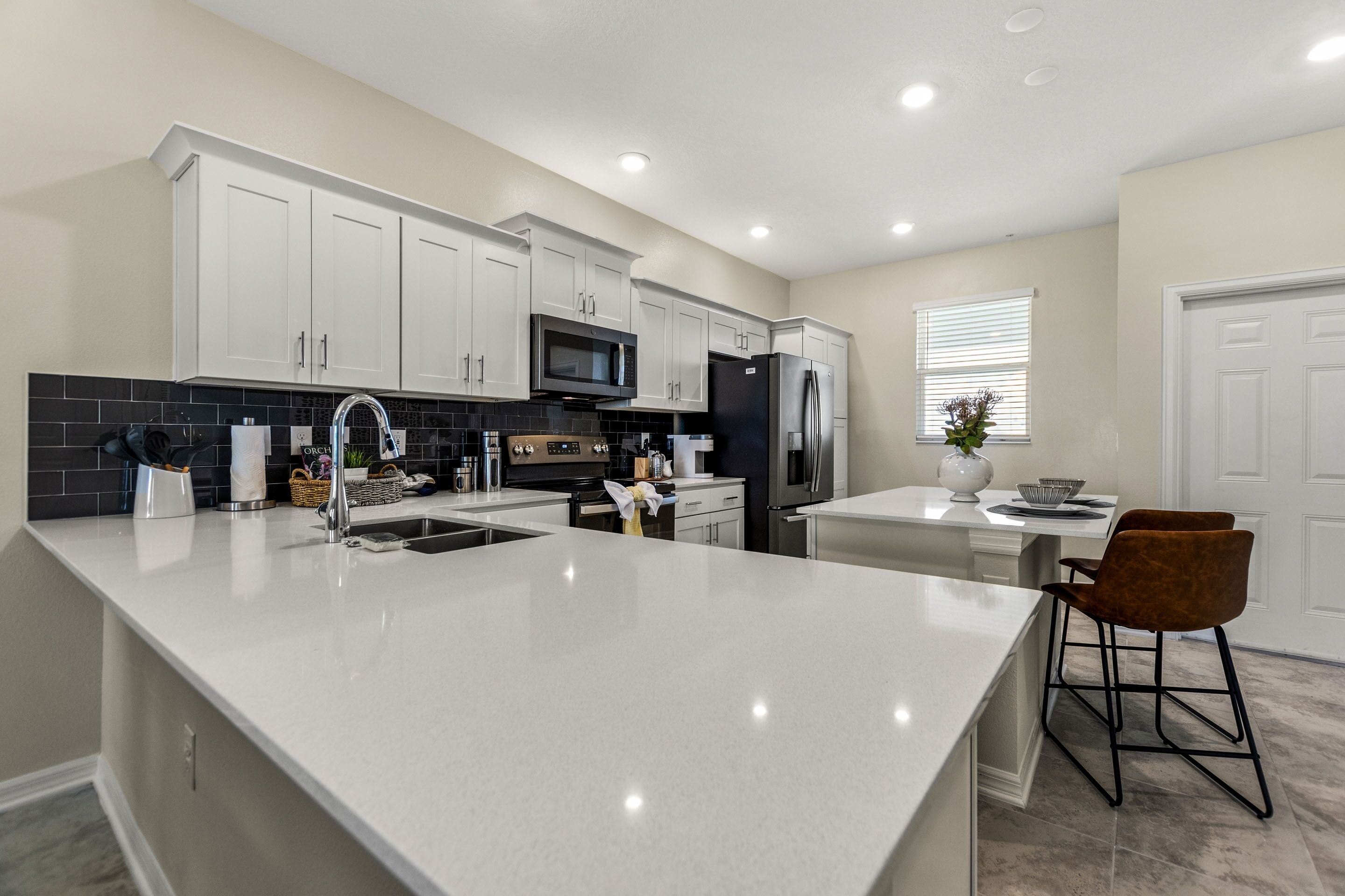 Una cocina moderna con armarios blancos, una isla grande, electrodomésticos de acero inoxidable y un taburete de bar.