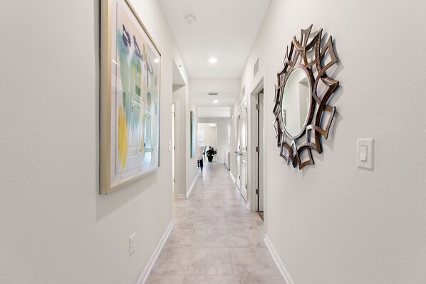 A hallway with a tiled floor, a large abstract painting on the left, and a decorative mirror on the right.