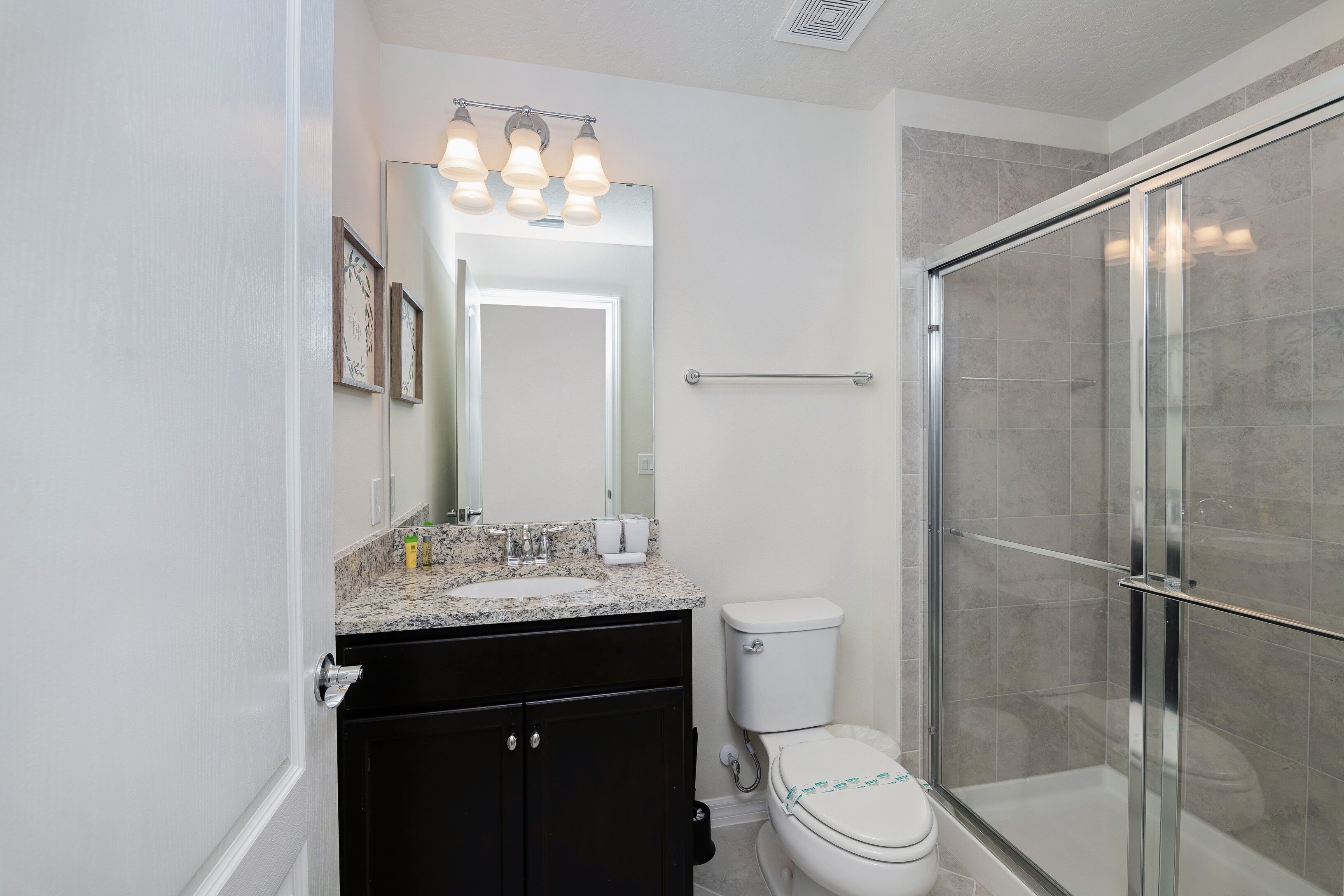 A modern bathroom with a granite countertop sink, a toilet, and a glass-enclosed shower.