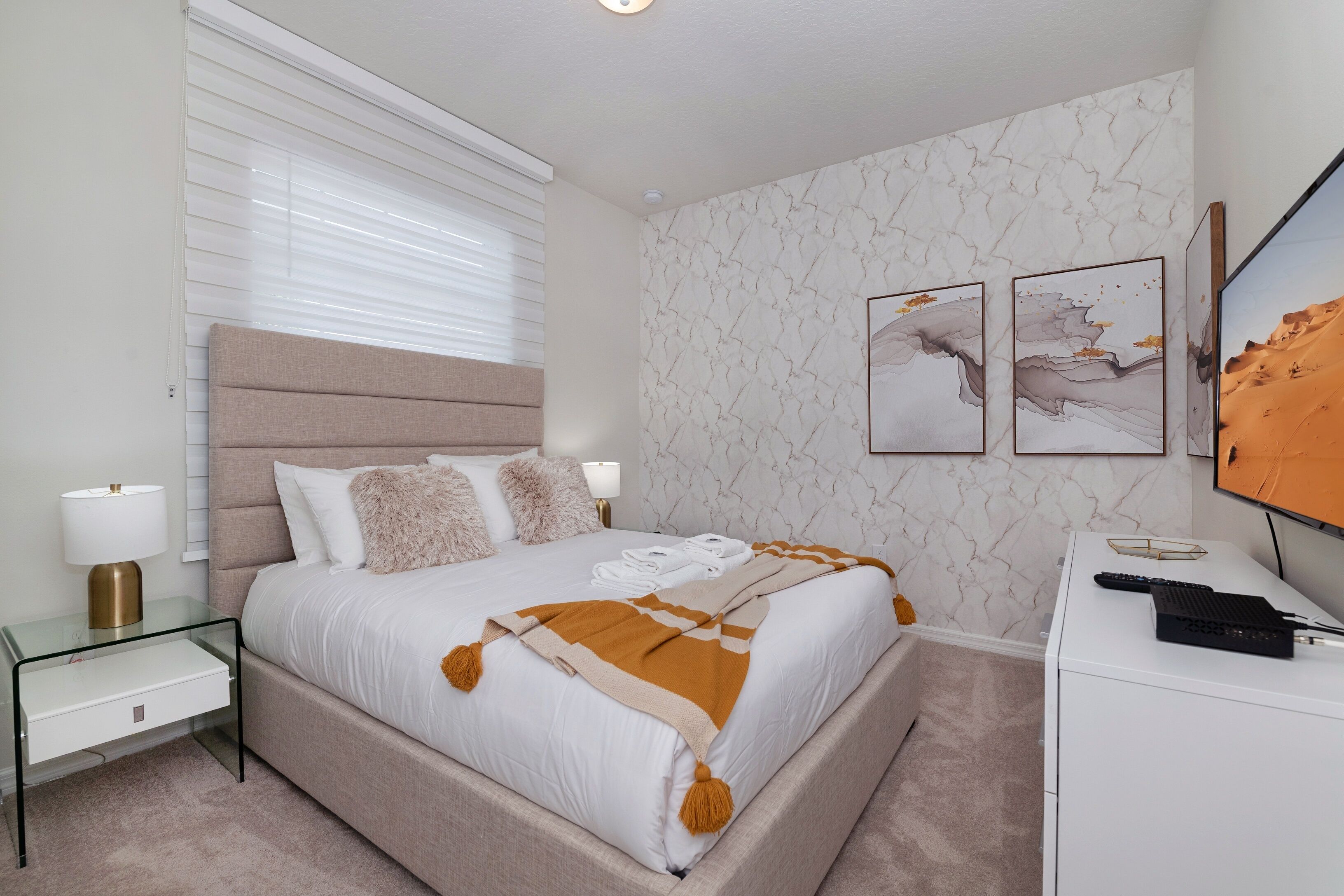 Une chambre moderne avec un grand lit, des tables de chevet, un bureau et un téléviseur fixé au mur.
