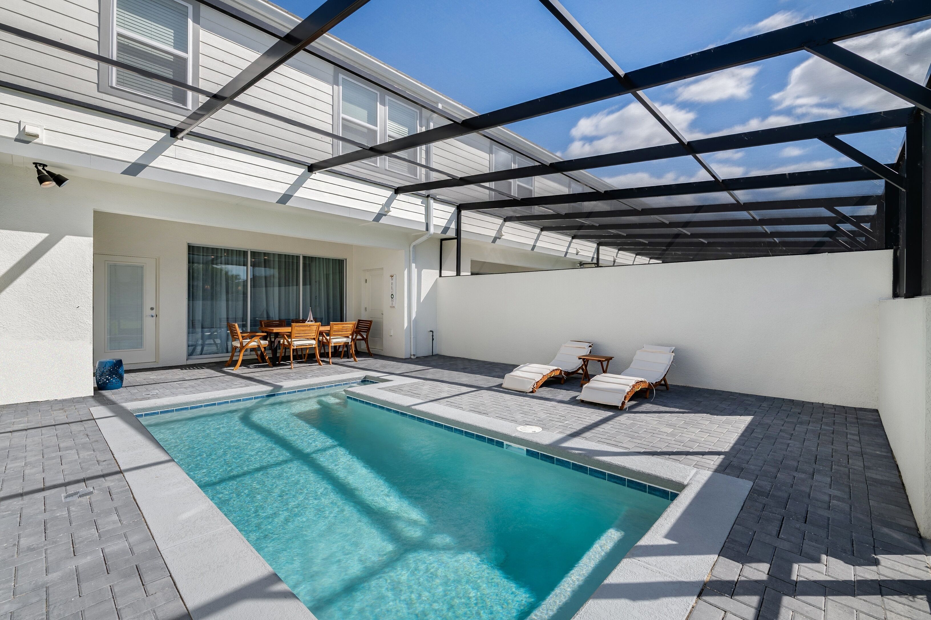 Ein moderner Poolbereich im Freien mit Glasdach, einer Sitzecke mit Stühlen und einem Tisch sowie einem klaren, blauen Pool.