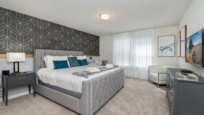 A modern bedroom with a large bed, bedside tables, a desk, and a chair. - Sun Traveler @ Solterra By Shine Villas #113 5 Bedroom Townhouse (Davenport)