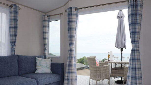 A room with a sofa, a table, and a view of the sea through a window. - The Retreat (Budleigh Salterton)
