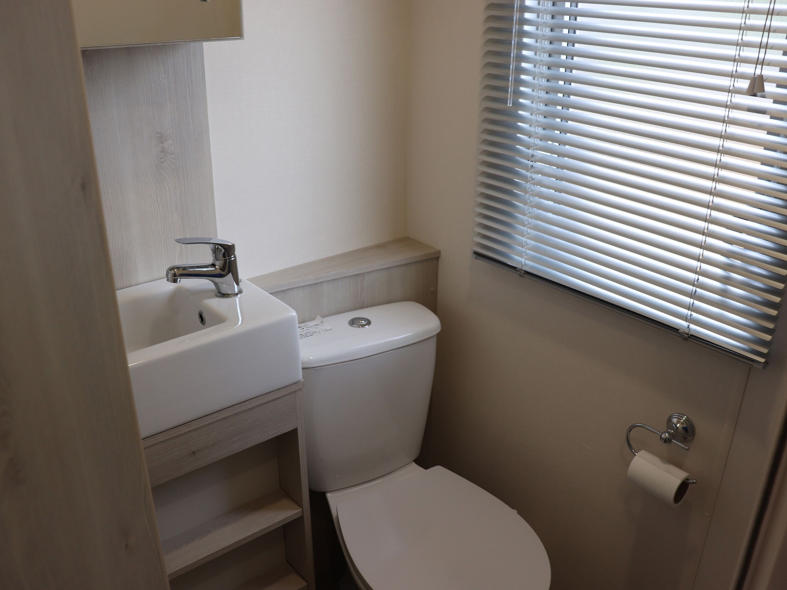 Et lille, moderne badeværelse med vask, toilet og vindue med persienner.