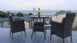 A deck with wicker chairs and a table, overlooking a coastal view. - The Retreat (Budleigh Salterton)
