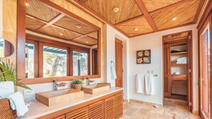 Un baño moderno con tocador de madera, ventanas amplias y techo de bambú.