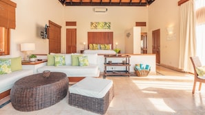Amplia sala de estar con techo de madera alta, un conjunto de sofás centrales, un otoman de mimbre y una pequeña mesa con objetos decorativos.