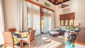 A spacious living area with a dining table, wicker chairs, a sofa, and a coffee table. Large windows with sheer curtains allow natural light to fill the room. - Bungallow 2 People Private Pool and Garden (Punta Cana)