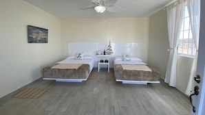 Une chambre avec deux lits, un ventilateur de plafond, une table de chevet et une fenêtre avec des rideaux.