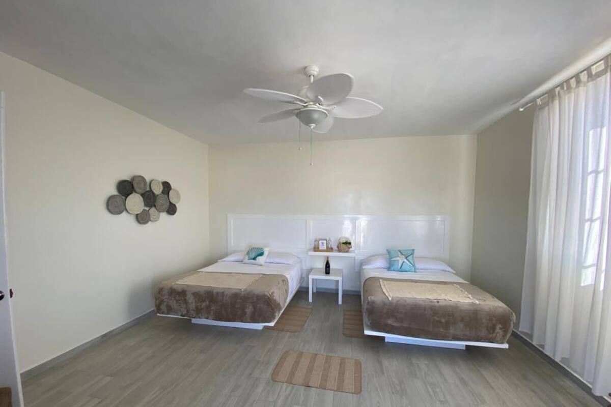 Een kamer met twee bedden, een plafondventilator, een klein tafeltje en een decoratie aan de muur.