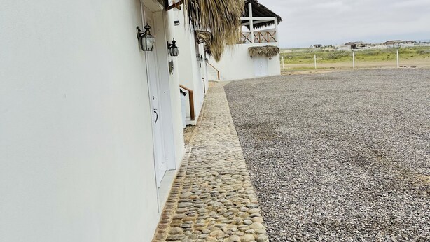 Un bâtiment blanc avec un chemin de pierre menant à une construction dont le toit est recouvert de chaume.