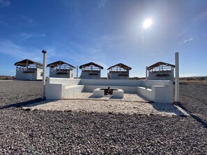 A row of white cabins with thatched roofs, arranged in a line on a gravel surface, under a clear blue sky. - Villas Capitan Petter (Punta Abreojos)