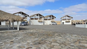 Une zone pavée de pierres, avec des constructions à toits de chaume, une voiture et une personne debout.