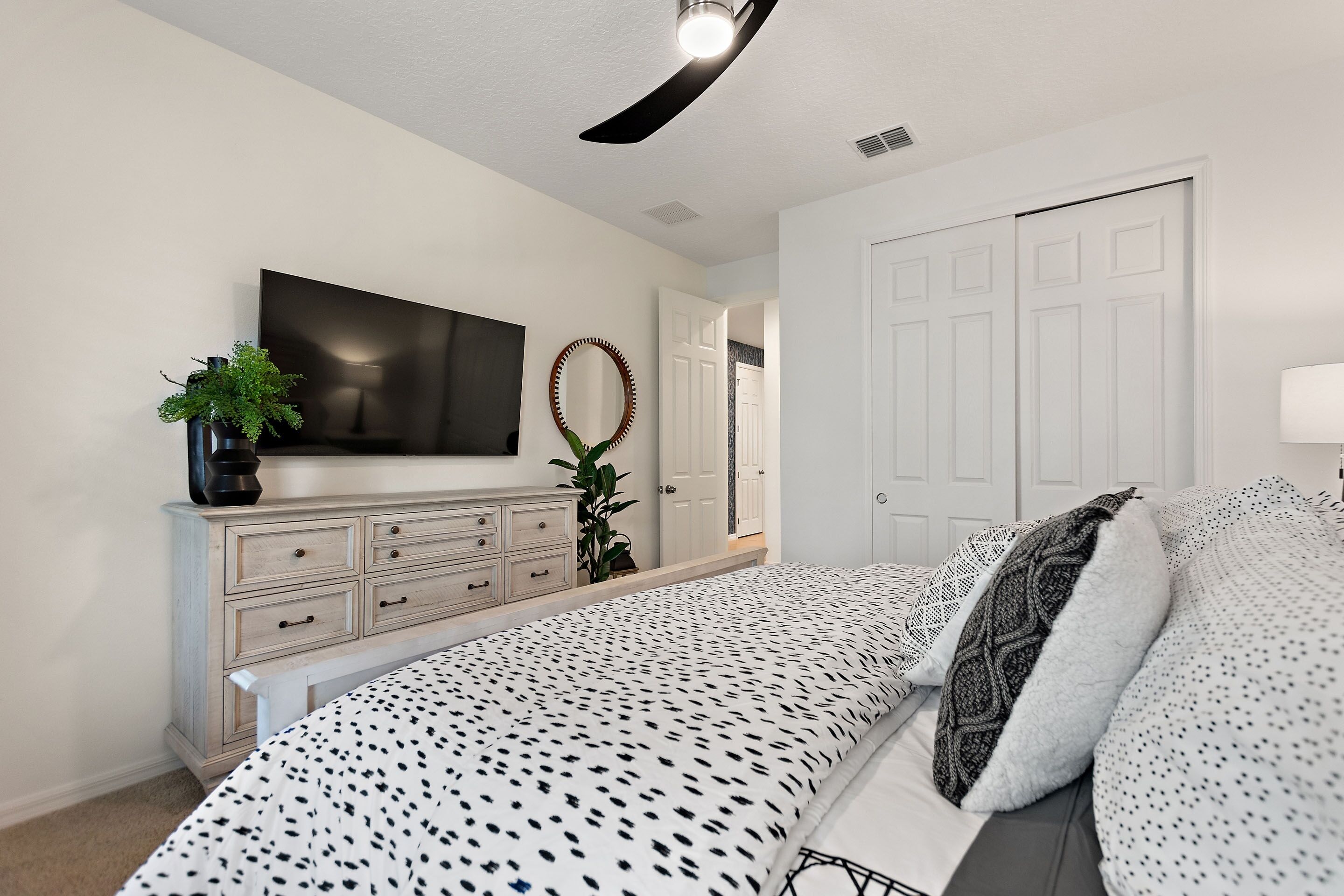 A bedroom with a bed, dresser, TV, and a door.