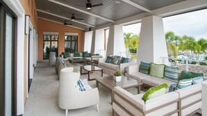 Een beschut buitengebied met banken, stoelen en tafels, met uitzicht op het strand en palmbomen.