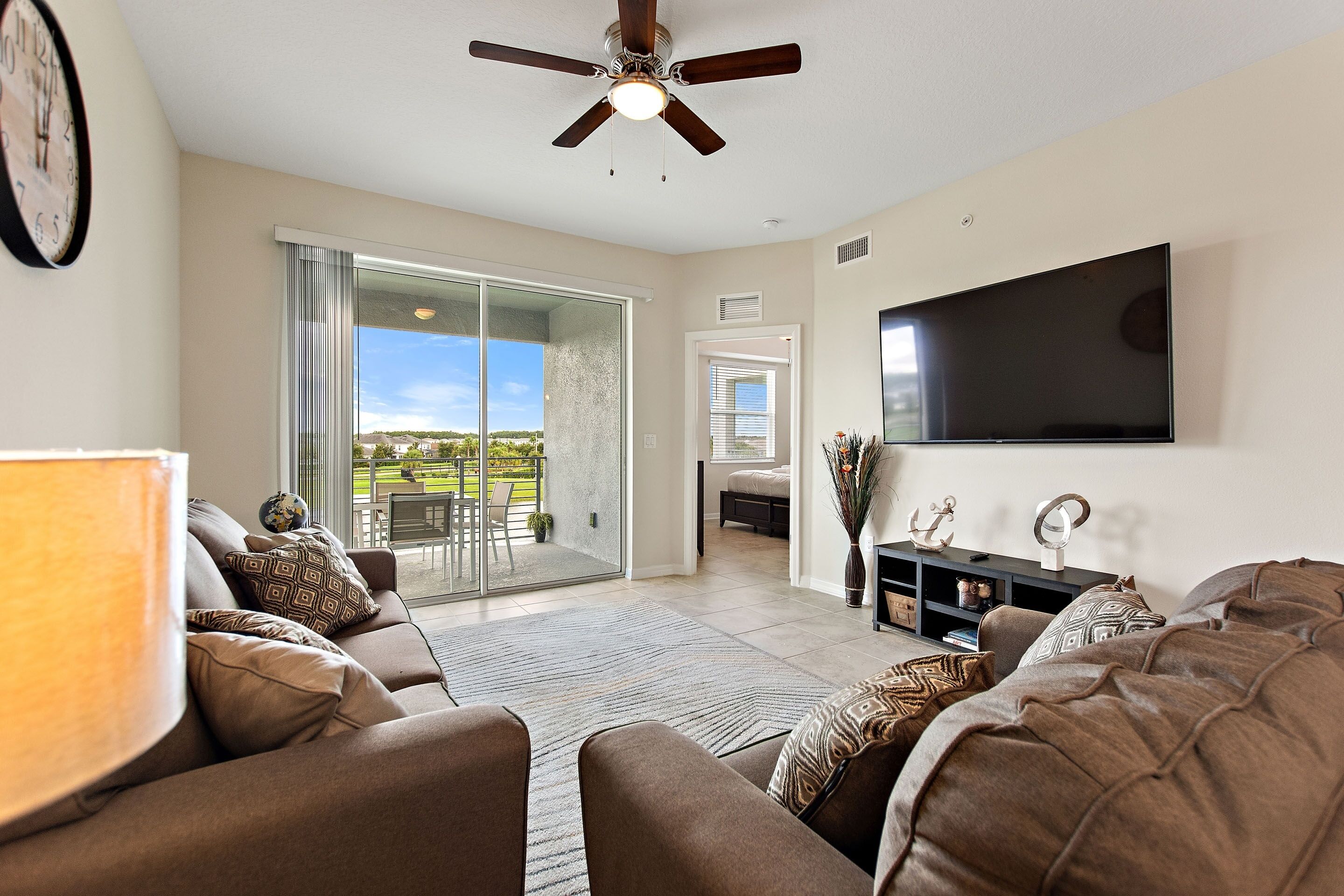 A living room with a ceiling fan, a flat-screen TV, a sofa, and a sliding glass door leading to a patio.