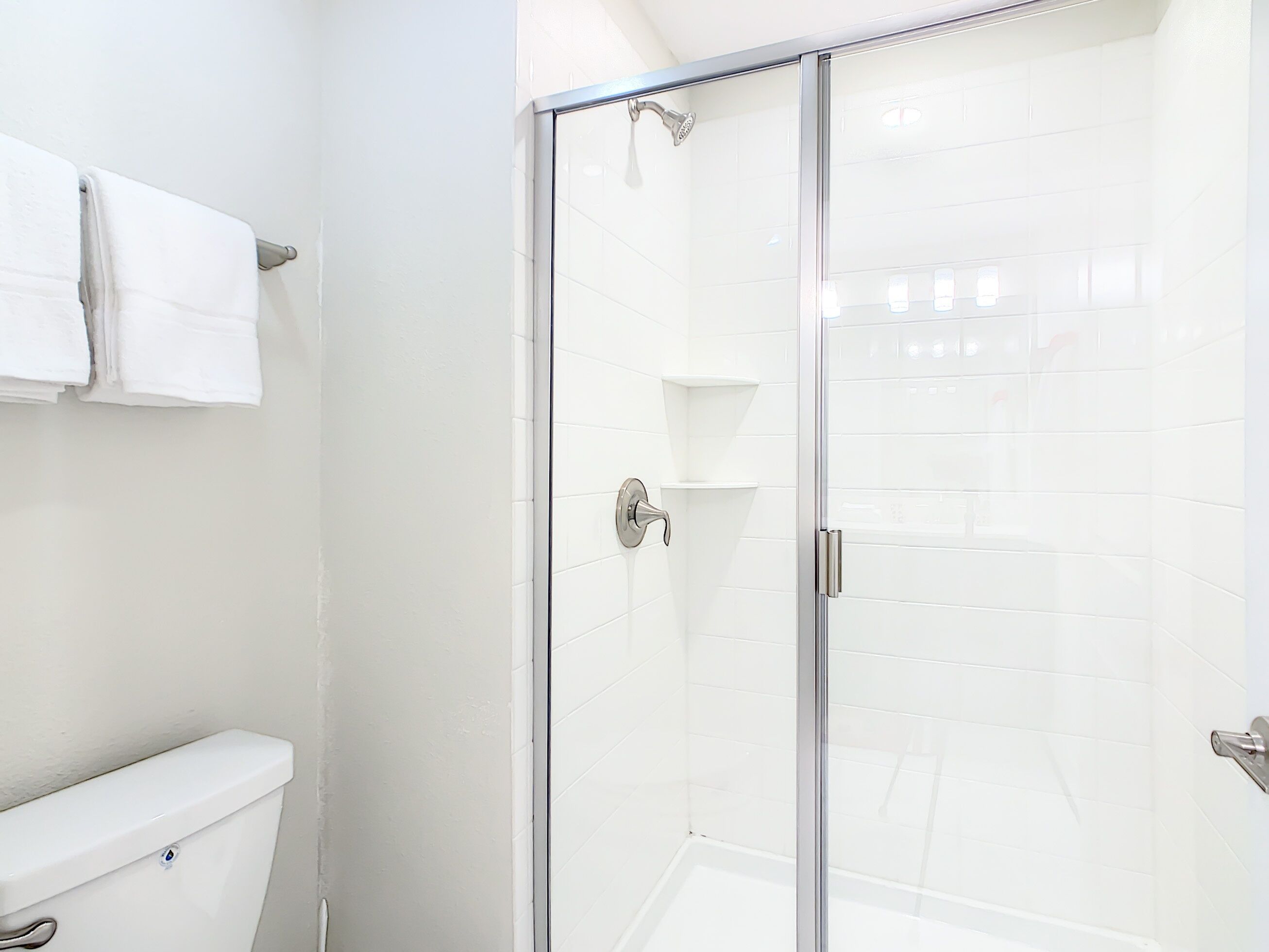 Une salle de bain avec une douche à parois de verre, des carreaux blancs et des toilettes.