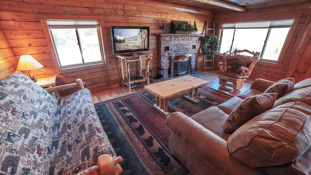 A cozy log cabin interior with a fireplace, a television mounted on the wall, and a large window providing natural light. - Rocky Mountain Retreat 2 Three Bedroom Cabin with Beautiful Views and Personal Hot Tub. 3 Cabin (Estes Park)