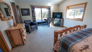 A cozy room with a bed, a wooden dresser, a leather chair, a fireplace, and a television. - Rocky Mountain Retreat 2 Three Bedroom Cabin with Beautiful Views and Personal Hot Tub. 3 Cabin (Estes Park)