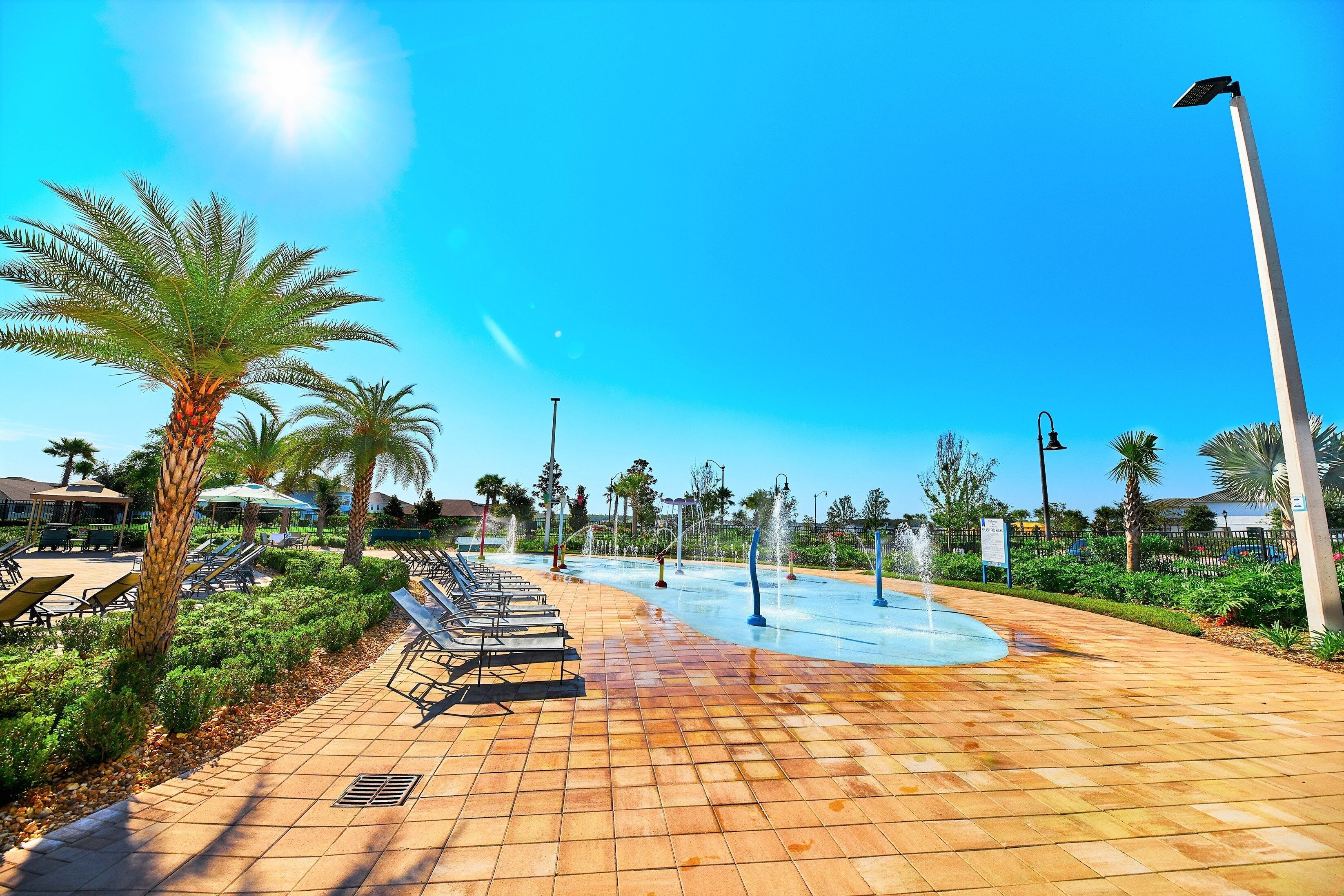 A sunny outdoor area with a water feature, palm trees, and lounge chairs.