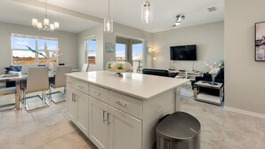 A spacious kitchen with a central island, pendant lights, and a dining area with chairs and a table. - Fireworks @ Night -storey Lake By Shine Villas 709 2 Bedroom Apts (Kissimmee)