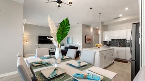 A modern kitchen with white cabinets, a black refrigerator, and a dining area with a white table set for four. - Fireworks @ Night -storey Lake By Shine Villas 709 2 Bedroom Apts (Kissimmee)