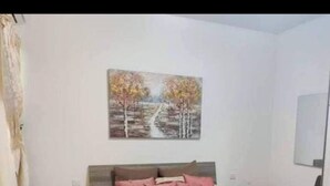 A bedroom with a bed, pillows, a nightstand, a chair, and a painting on the wall. - Beautiful 2 Bed Apartment in Għajnsielem (Ghajnsielem)