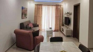 A modern living room with a sofa, a dining table, and a TV. - Beautiful 2 Bed Apartment in Għajnsielem (Ghajnsielem)
