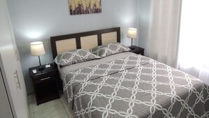 Quarto bem arrumado com cama, duas mesas de cabeceira com luminárias, um ar condicionado fixado na parede e um quadro sobre a cama.