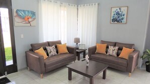 Uma sala de estar com dois sofás marrons, uma mesa de centro, uma luminária e um vaso com planta.