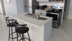 Uma cozinha moderna com ilha central, eletrodomésticos de aço inoxidável e banquetas.