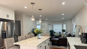 A modern kitchen with a central island, stainless steel appliances, pendant lighting, and a seating area with a sofa and chairs.