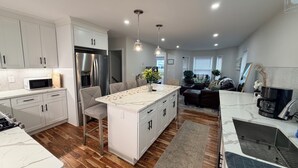 A modern kitchen with white cabinets, a central island, a refrigerator, and a dining area with chairs.