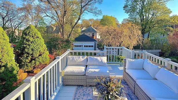 A deck with a white railing, a wicker sofa, and a patterned rug.